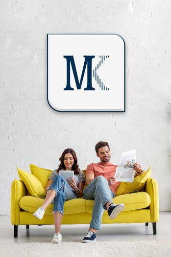 Junge Frau und junger Mann sitzen lächelnd auf einem limettenfarbenen Sofa. Der Mann liest eine Zeitung, die Frau hält ein weißes Tablet.